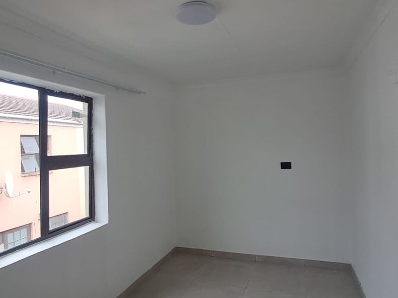 A clean, empty bedroom featuring tiled flooring, a neutral white finish, and an aluminium-framed window.
