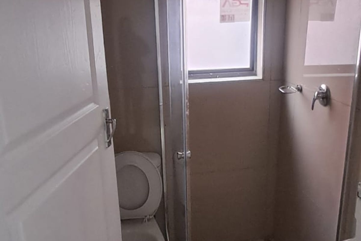 A compact bathroom featuring a glass-enclosed shower, toilet, and basin with neutral wall and floor tiling.