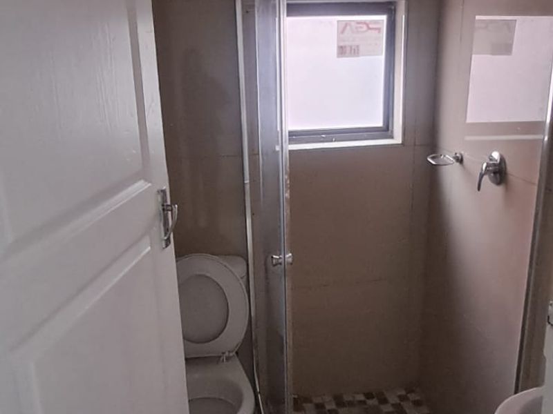 A compact bathroom featuring a glass-enclosed shower, toilet, and basin with neutral wall and floor tiling.