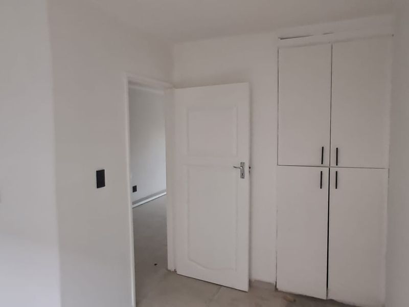 A clean, empty hallway featuring a built-in storage cupboard and access to an adjacent room.