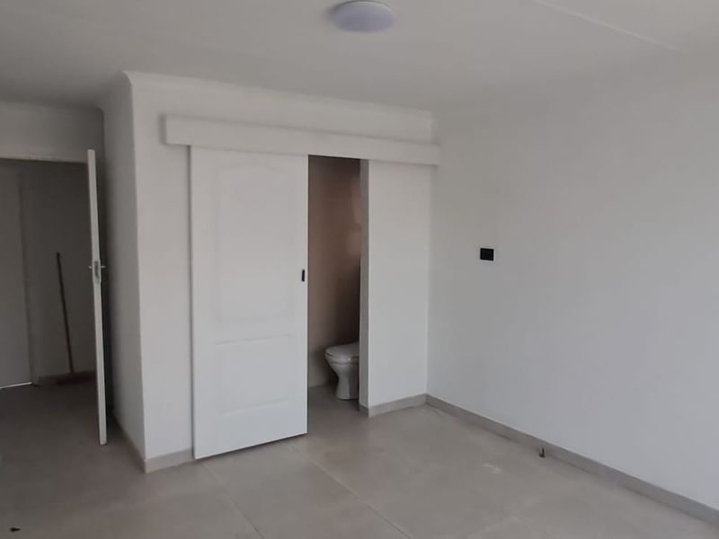 A clean, empty bedroom featuring neutral tiled flooring, a sliding door leading to an en-suite bathroom, and a simple, modern interior finish.