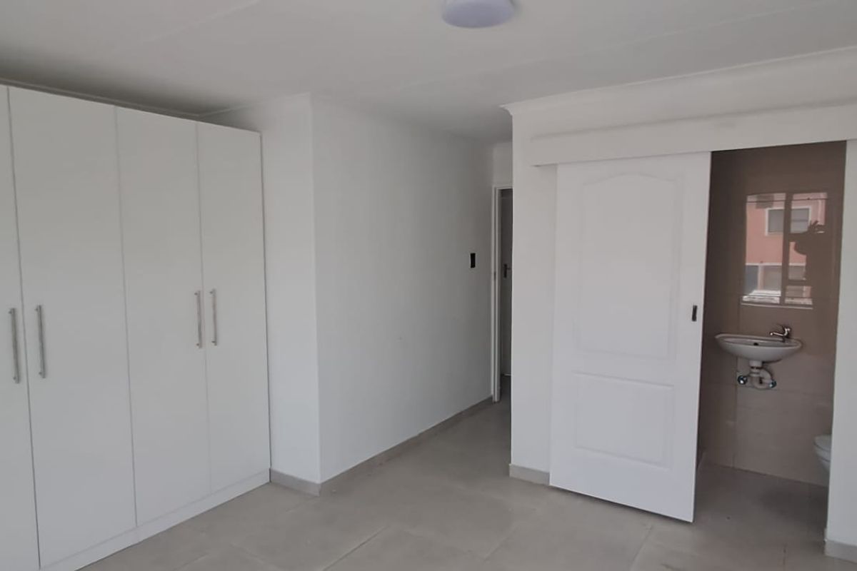 A clean, modern bedroom featuring built-in cupboards, neutral tiled flooring, and a sliding door leading to an en-suite bathroom.
