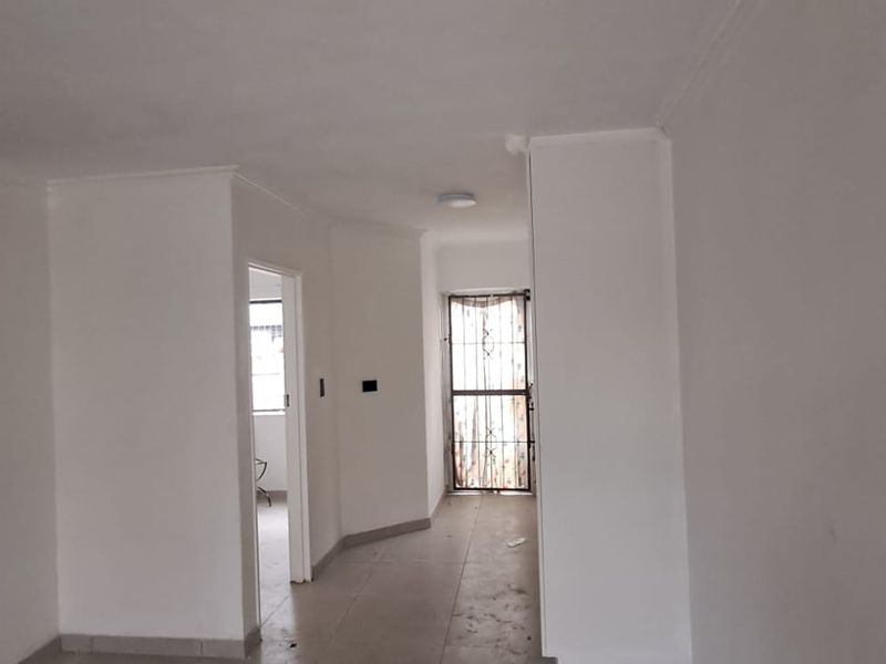An empty hallway featuring tiled flooring, a staircase, and a security gate leading to an exterior entrance.