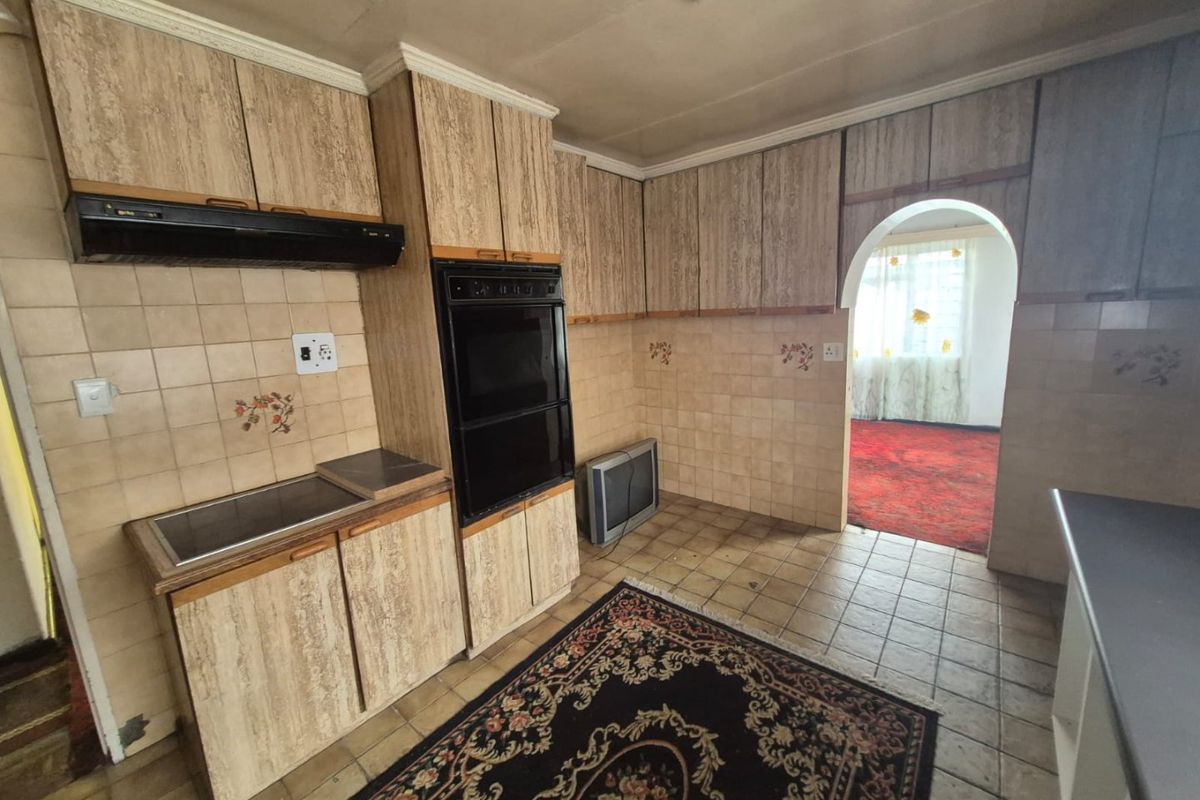 A dated kitchen featuring original wood-grain cabinetry, built-in oven, extractor fan, and tiled surfaces, offering significant potential for a modern renovation.