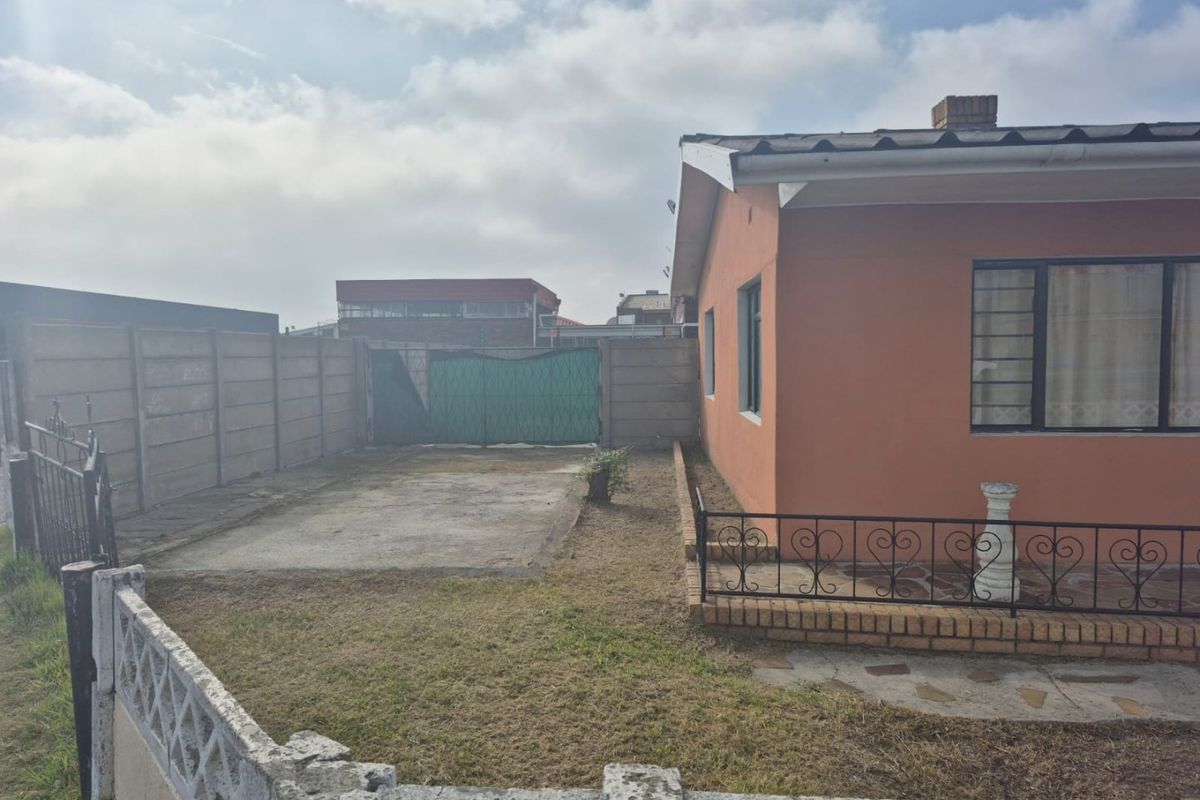 Rear exterior view of the property featuring a concrete patio area, precast boundary walls, and wrought iron fencing with a small garden space.