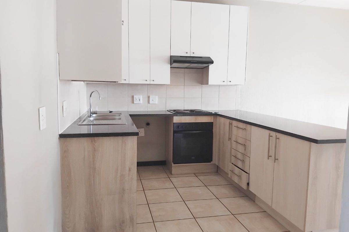 A clean, modern kitchen featuring light wood-finish cabinetry, dark granite countertops, built-in oven and hob, and neutral tiled flooring.