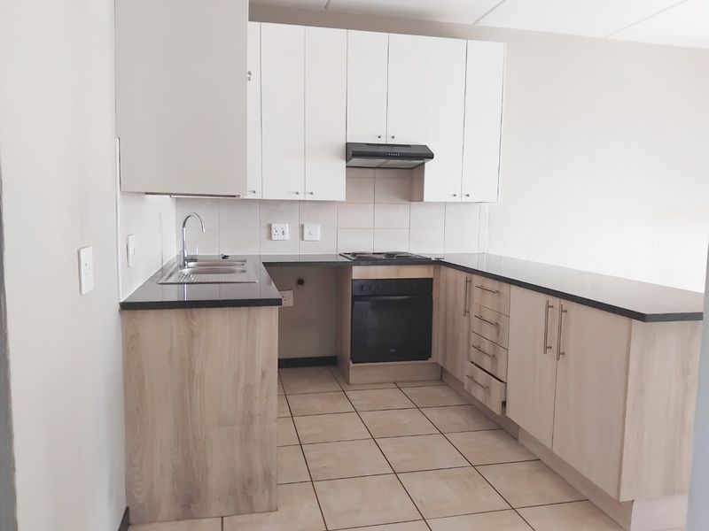 A clean, modern kitchen featuring light wood-finish cabinetry, dark granite countertops, built-in oven and hob, and neutral tiled flooring.
