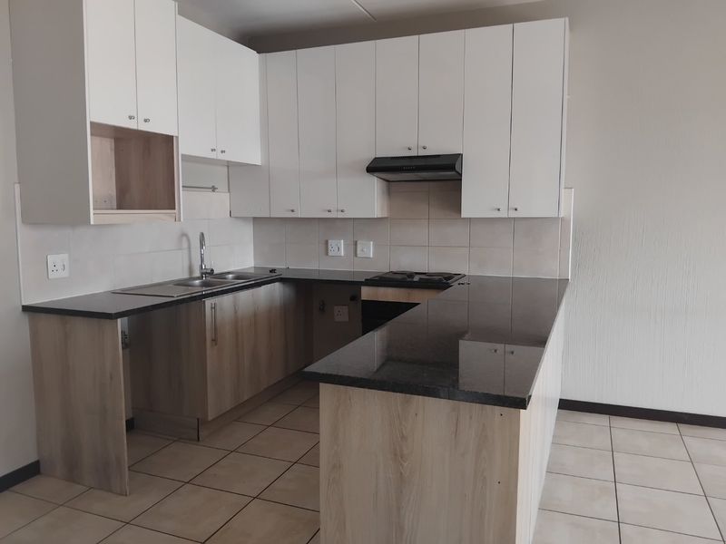 Modern kitchen featuring light wood-finish cabinetry, dark granite countertops, a built-in hob with extractor fan, and neutral tiled flooring.