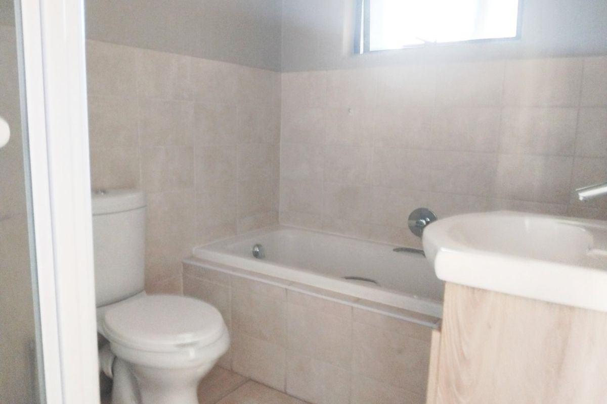 A functional bathroom featuring a bathtub, toilet, and vanity with neutral wall and floor tiling.