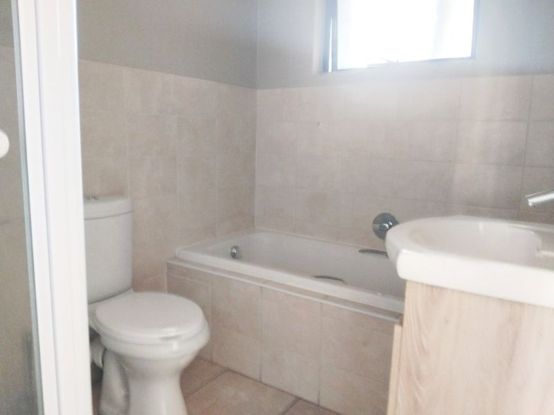 A functional bathroom featuring a bathtub, toilet, and vanity with neutral wall and floor tiling.