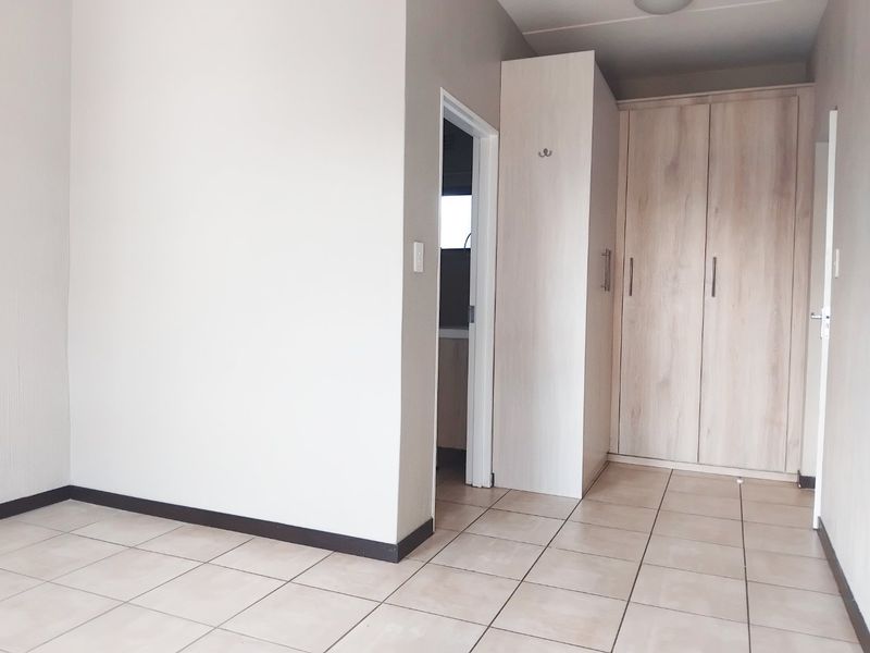 A clean, empty bedroom featuring light wood-finish built-in cupboards and neutral tiled flooring, offering a versatile space ready for personalization.