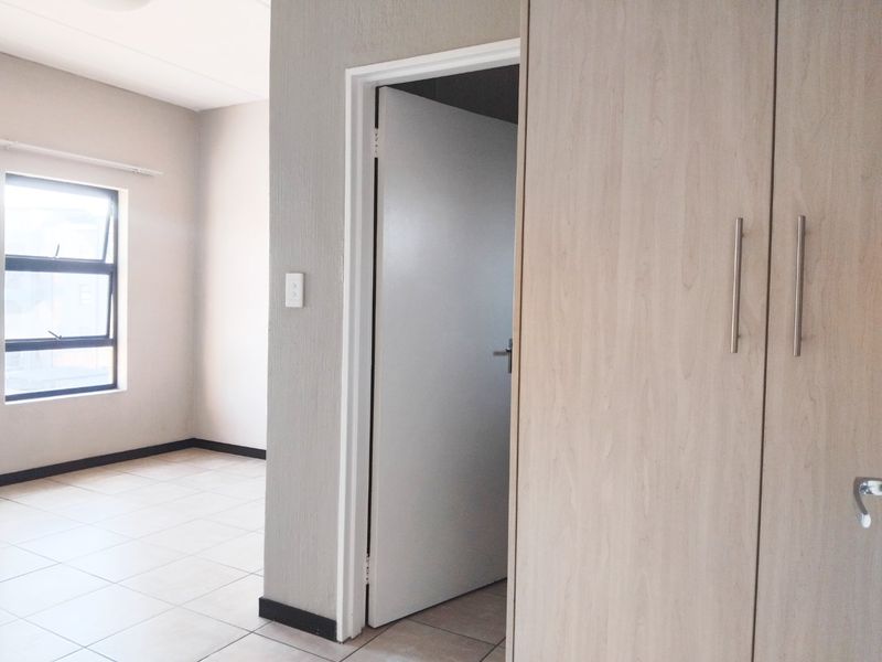 A bright, empty bedroom featuring neutral tiled flooring, built-in wooden cupboards, and a large window allowing for natural light.