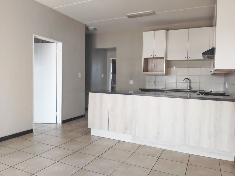 Open plan kitchen featuring light wood-look cabinetry, dark stone countertops, tiled backsplash, and neutral floor tiles in a clean, vacant space.