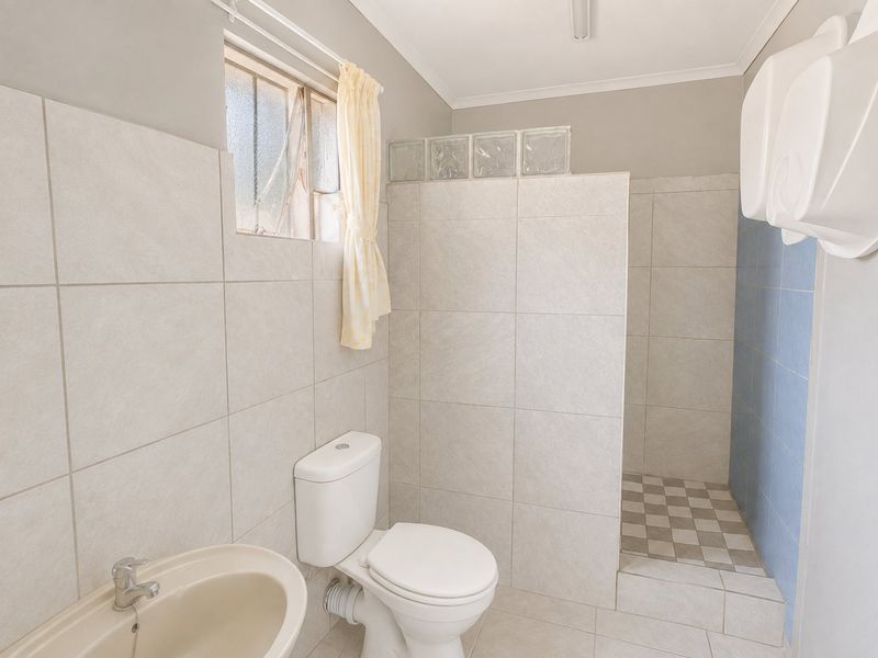 A functional bathroom featuring a walk-in shower, toilet, and basin with neutral wall tiling and a glass block feature window.