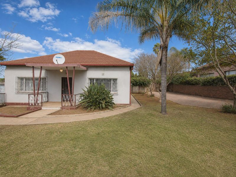 Front view of a single-story house featuring a tiled roof, covered porch, security bars on windows, and a spacious front garden with a paved driveway.