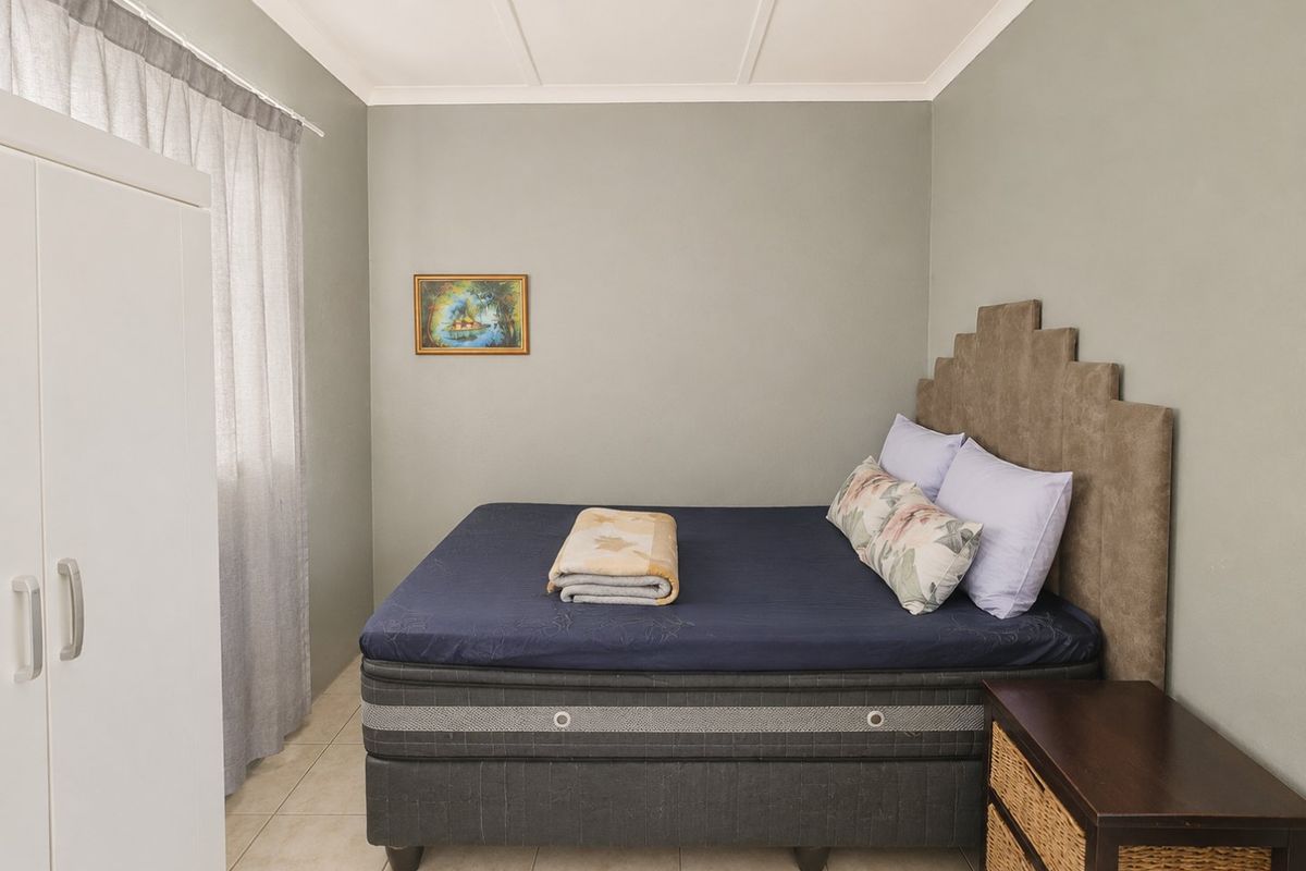 A functional bedroom featuring neutral wall tones, tiled flooring, and a built-in wardrobe, offering a clean and simple living space.