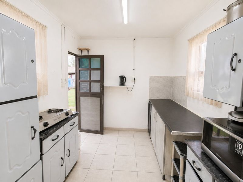 A functional kitchen featuring tiled flooring, built-in cabinetry, laminate countertops, and a gas hob, with direct access to the exterior.
