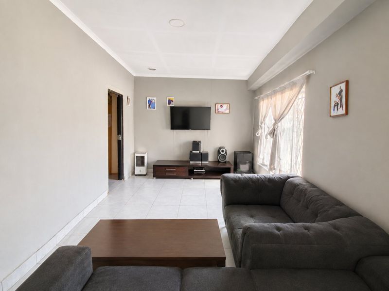A neutrally painted living room featuring tiled flooring, recessed ceiling lights, and a window fitted with a security gate.