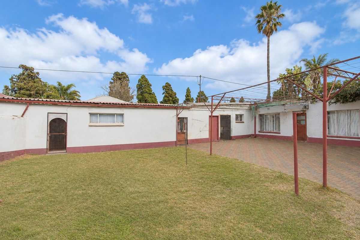 Rear exterior view featuring a paved courtyard, lawn area, and metal pergola structure attached to the main building.
