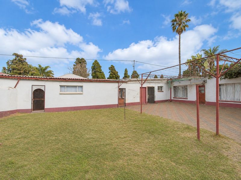 Rear exterior view featuring a paved courtyard, lawn area, and metal pergola structure attached to the main building.