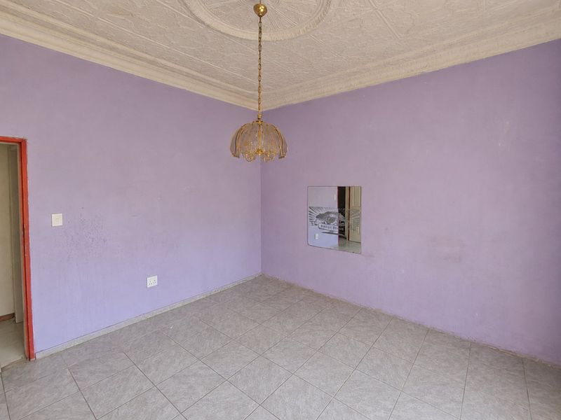 An empty living room featuring ceramic floor tiles, an ornate ceiling rose with decorative cornice, and a central pendant light fixture.