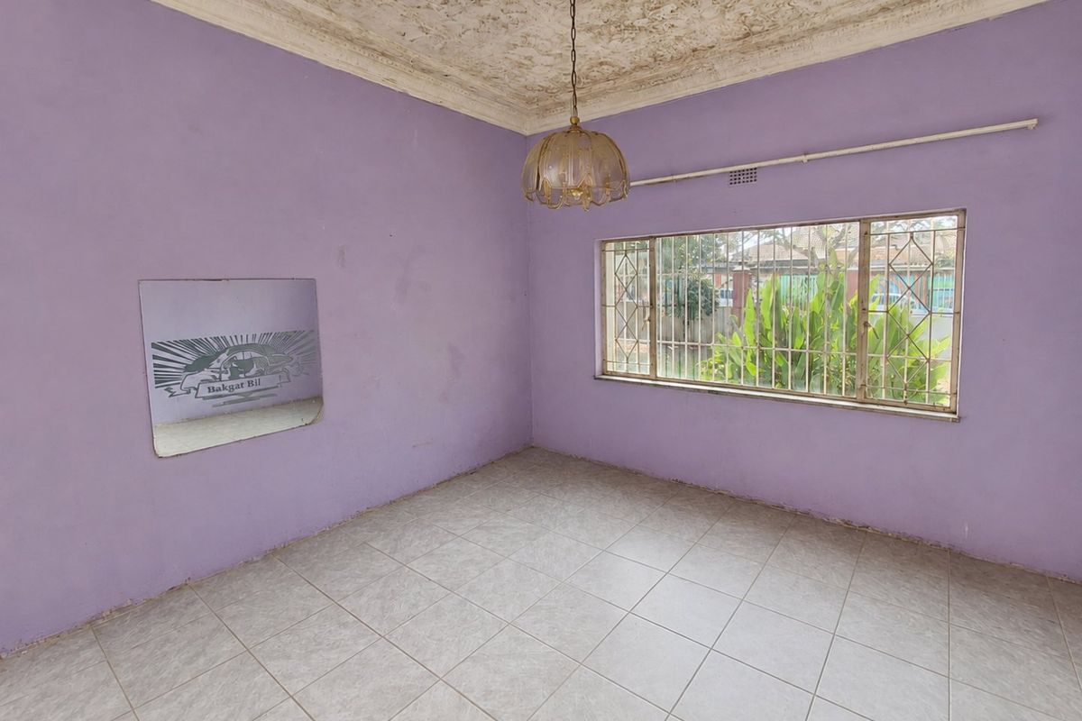An empty living room featuring original ornate ceiling detailing, tiled flooring, and large windows with security bars, awaiting a modern update.