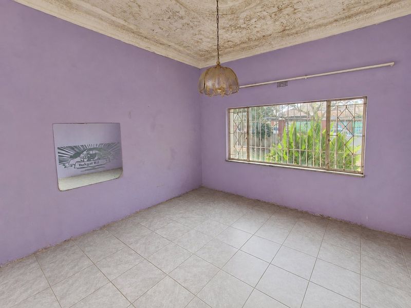 An empty living room featuring original ornate ceiling detailing, tiled flooring, and large windows with security bars, awaiting a modern update.