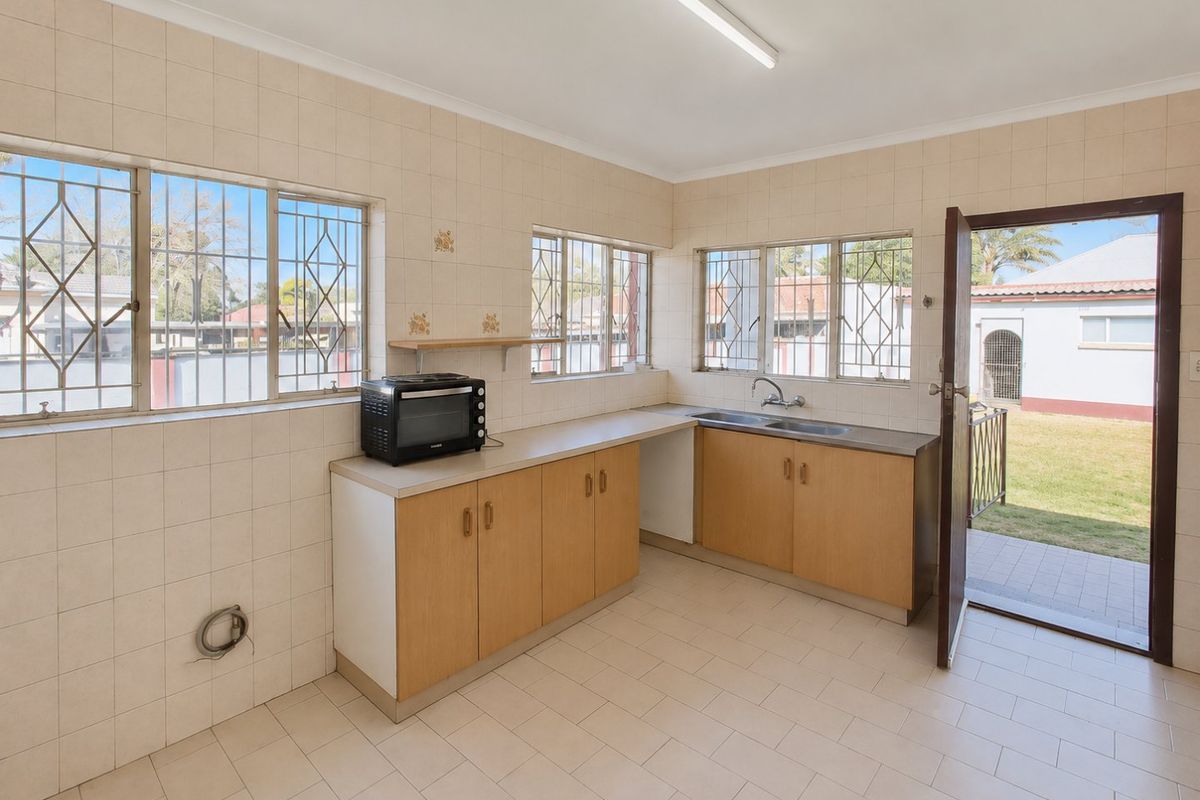 A functional kitchen space featuring tiled walls and flooring, built-in cabinetry, a double sink, and direct access to the rear garden.