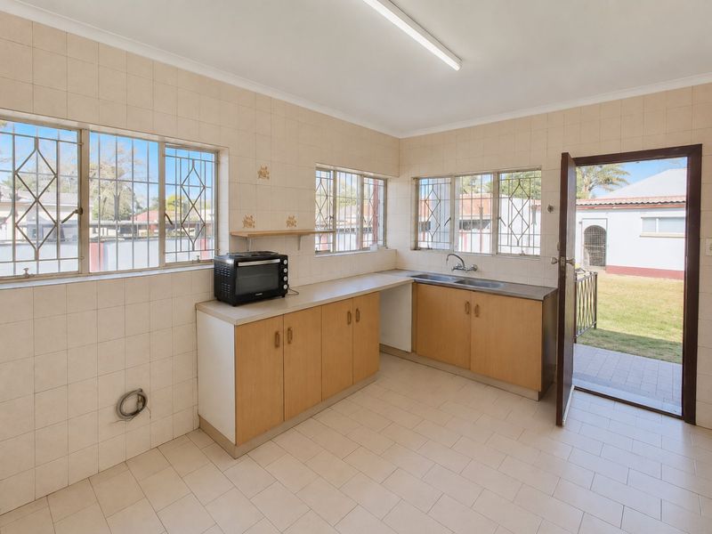 A functional kitchen space featuring tiled walls and flooring, built-in cabinetry, a double sink, and direct access to the rear garden.