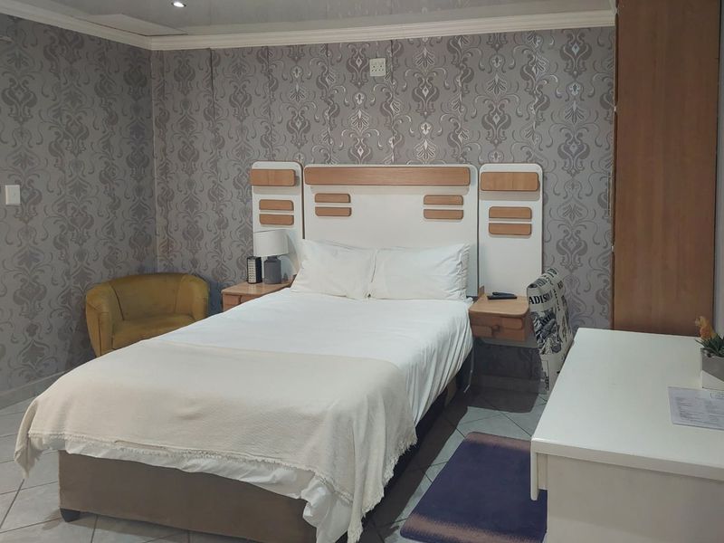 A bedroom featuring a built-in headboard, patterned wallpaper, and tiled flooring.