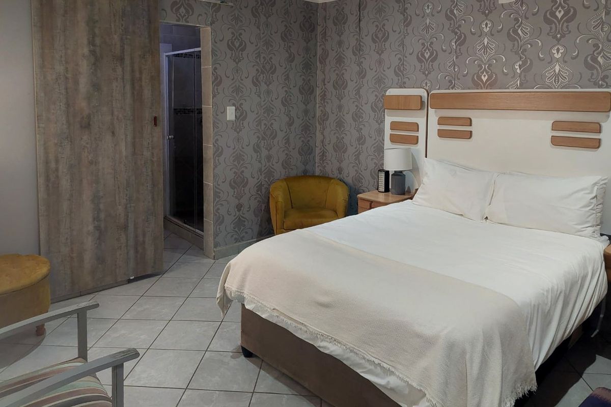 A bedroom featuring tiled flooring, patterned wallpaper, and a sliding door providing access to an en-suite bathroom.