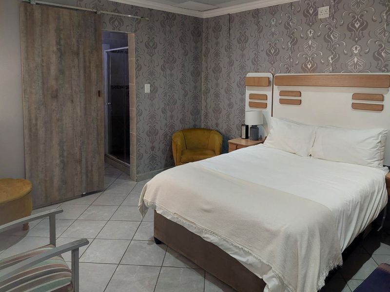 A bedroom featuring tiled flooring, patterned wallpaper, and a sliding door providing access to an en-suite bathroom.