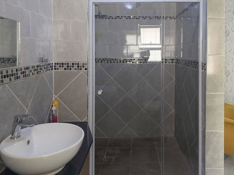 A modern bathroom featuring a vessel sink on a dark vanity countertop and a separate glass-enclosed shower with decorative mosaic tile accents.