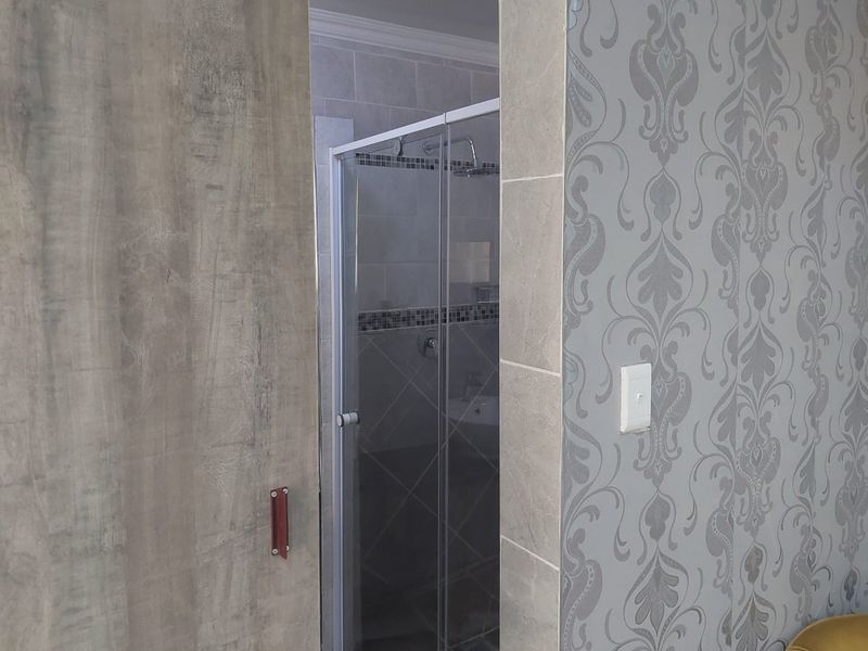 A view into a bathroom featuring a glass-enclosed shower with tiled walls and a modern sliding door entrance.
