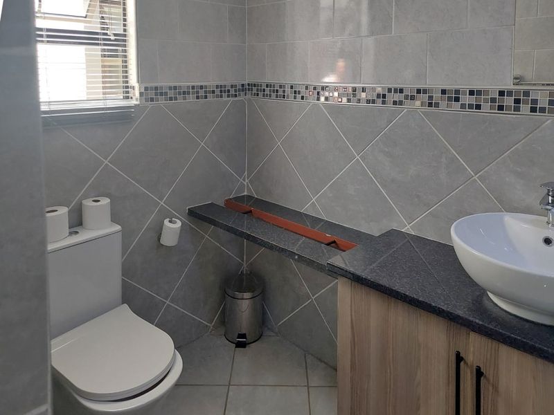 A bathroom featuring tiled walls, a vanity cabinet with a vessel sink, and a toilet. Note the missing section in the vanity countertop.