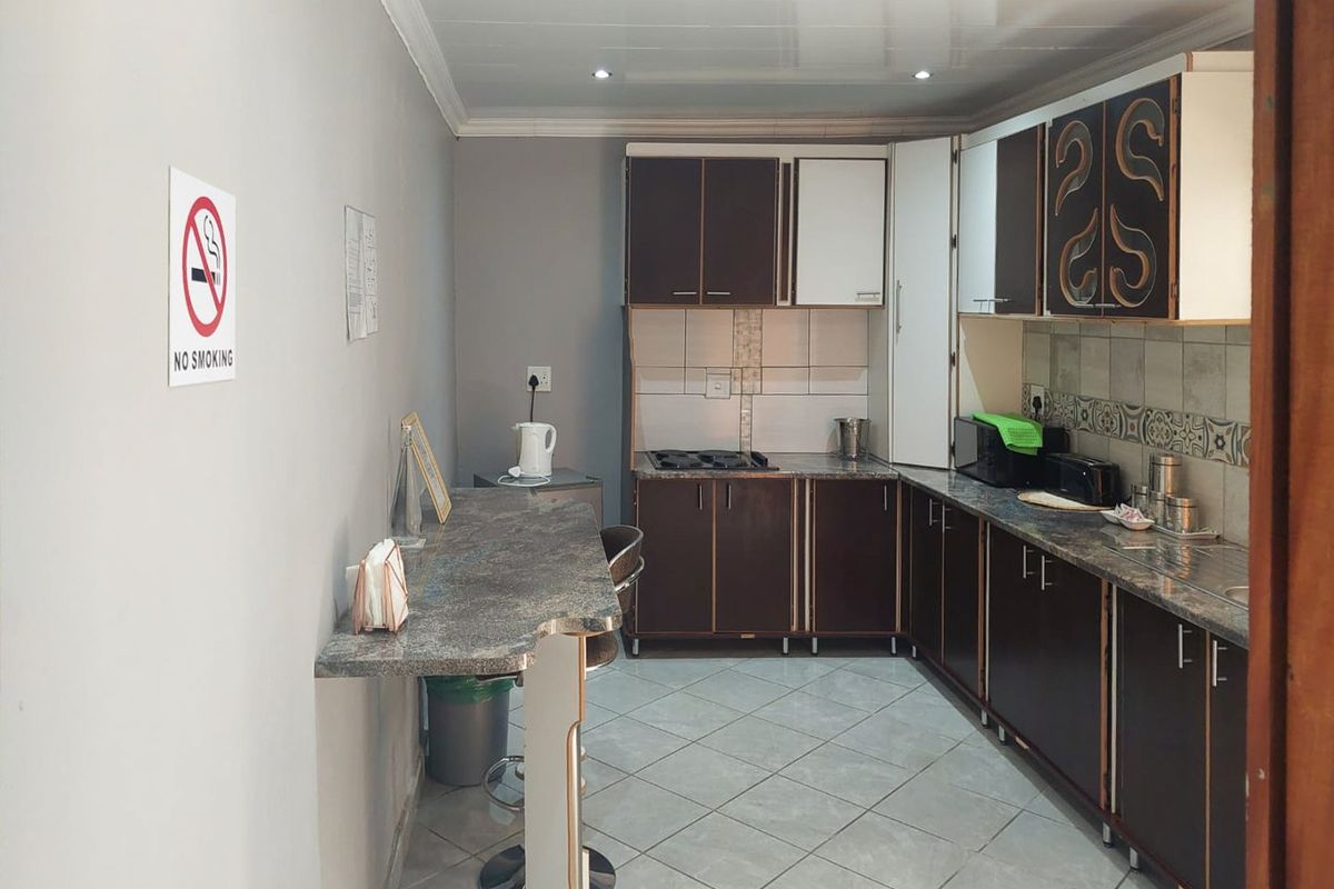 A functional kitchen featuring dark cabinetry, laminate countertops, a built-in hob, and tiled flooring with an integrated breakfast bar area.