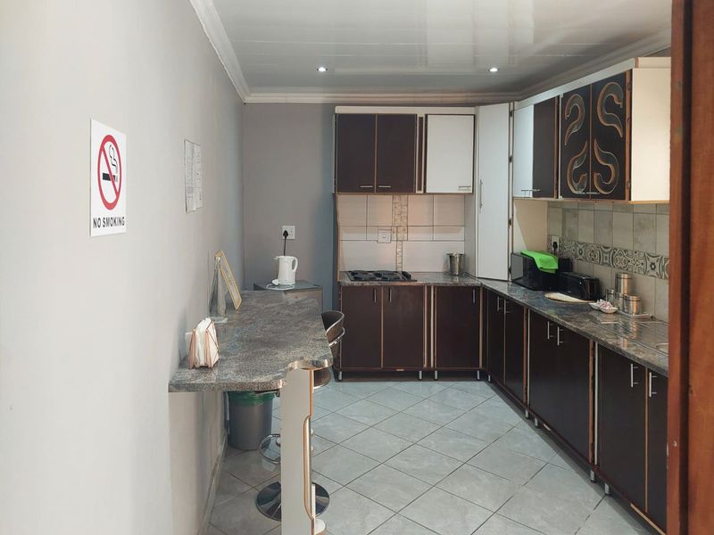 A functional kitchen featuring dark cabinetry, laminate countertops, a built-in hob, and tiled flooring with an integrated breakfast bar area.