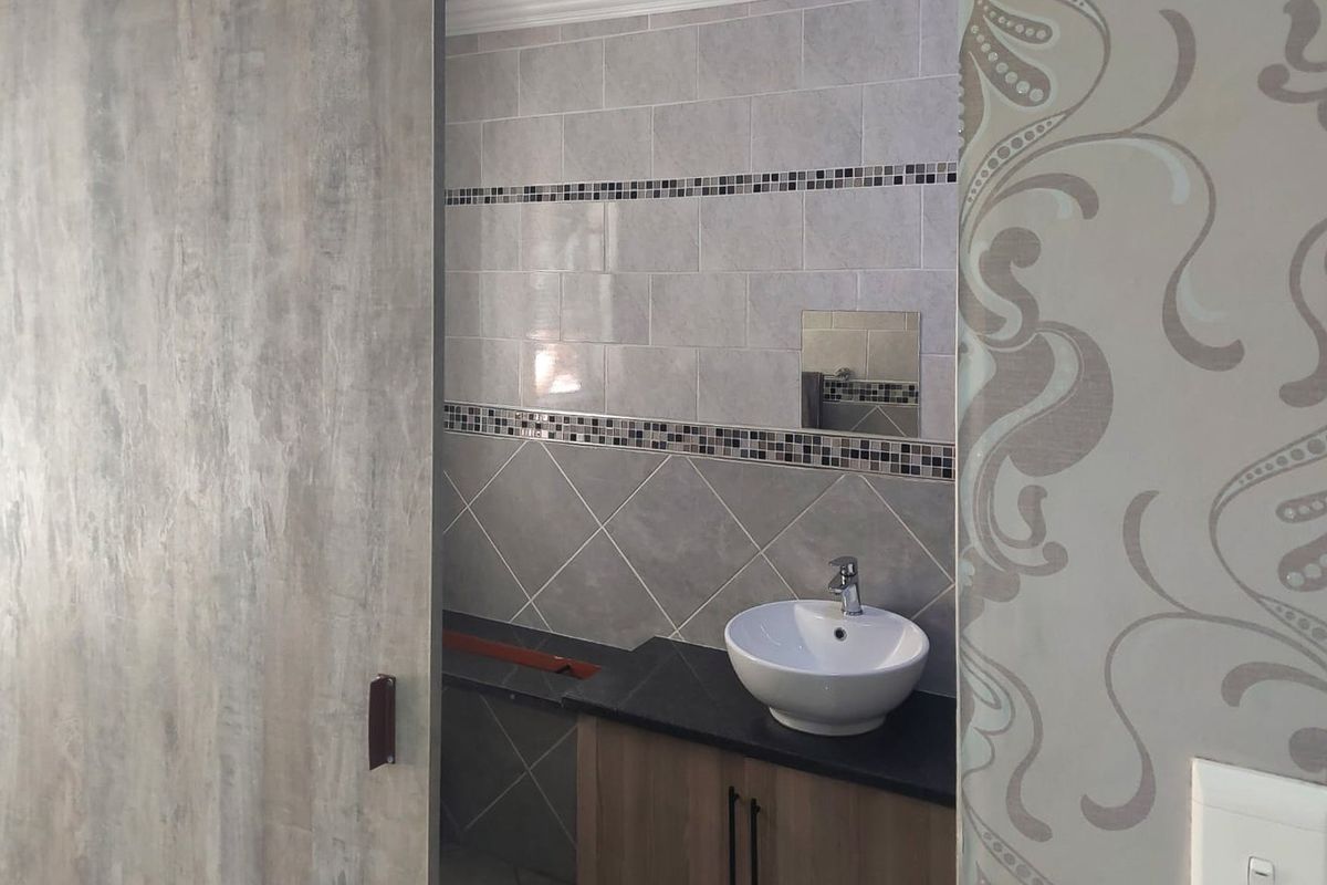 A compact bathroom featuring a modern vessel sink on a vanity cabinet, accented by decorative tiled walls and a sliding door entry.