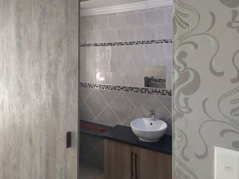 A compact bathroom featuring a modern vessel sink on a vanity cabinet, accented by decorative tiled walls and a sliding door entry.
