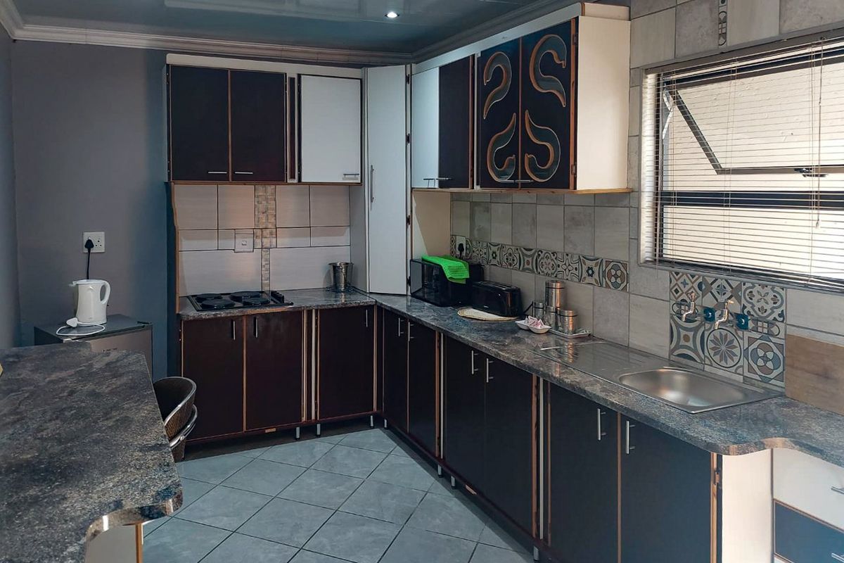 Functional kitchen featuring dark cabinetry, laminate countertops, a gas hob, and tiled backsplash with neutral floor tiling and recessed lighting.
