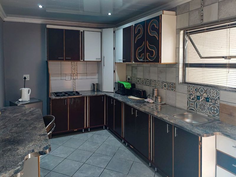 Functional kitchen featuring dark cabinetry, laminate countertops, a gas hob, and tiled backsplash with neutral floor tiling and recessed lighting.