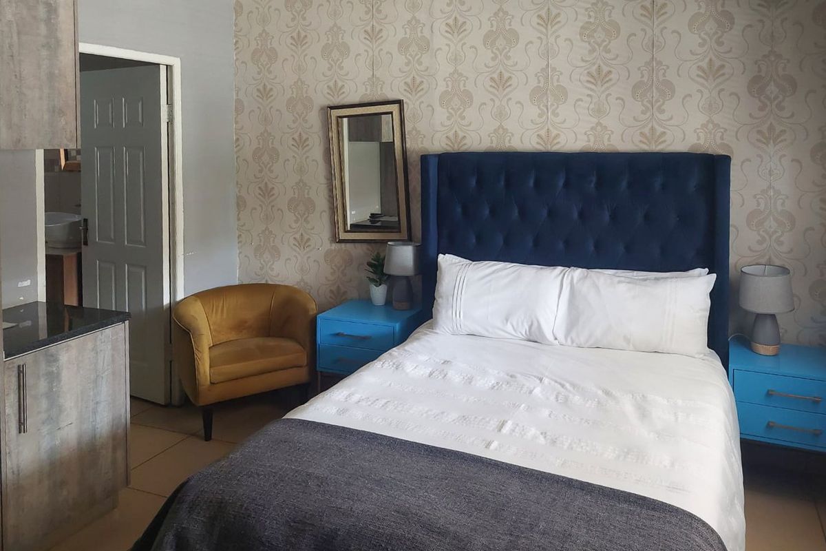 A well-maintained bedroom featuring tiled flooring and decorative wallpaper, with direct access to an adjoining bathroom.