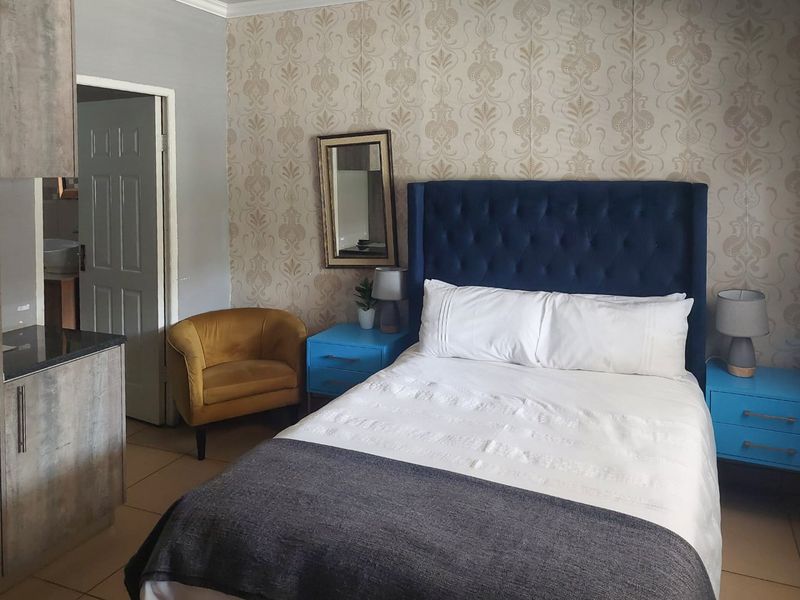 A well-maintained bedroom featuring tiled flooring and decorative wallpaper, with direct access to an adjoining bathroom.