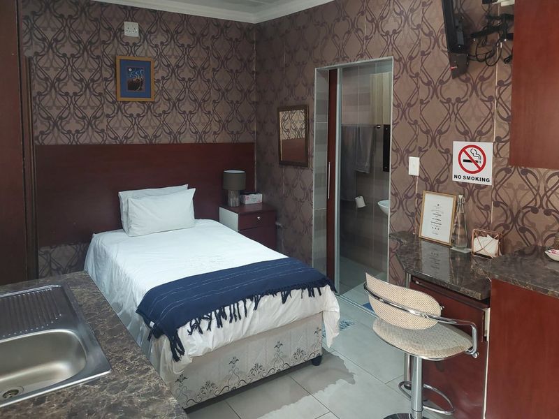 Compact open-plan studio apartment featuring a kitchenette with sink, tiled flooring, and an en-suite bathroom with a sliding door.