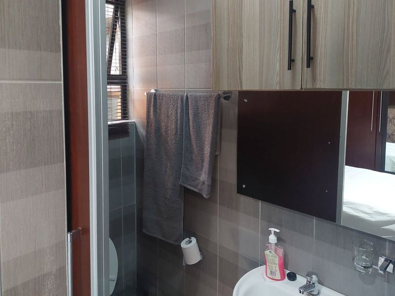A compact bathroom featuring tiled walls, a wall-mounted vanity cabinet, a basin with a mixer tap, and a mirror.