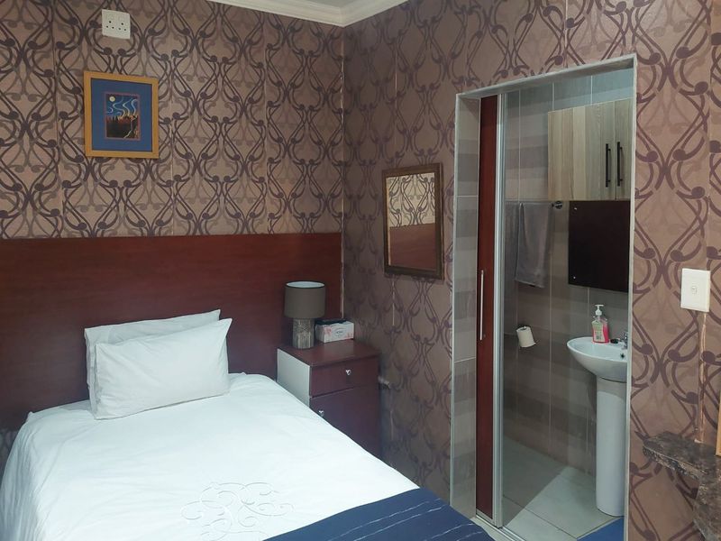A bedroom featuring a built-in headboard and an integrated en-suite bathroom with a pedestal sink and sliding door access.