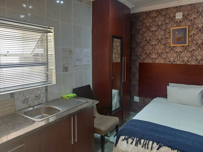 A compact bedroom featuring a built-in wardrobe and a small kitchenette area with a sink and tiled splashback.