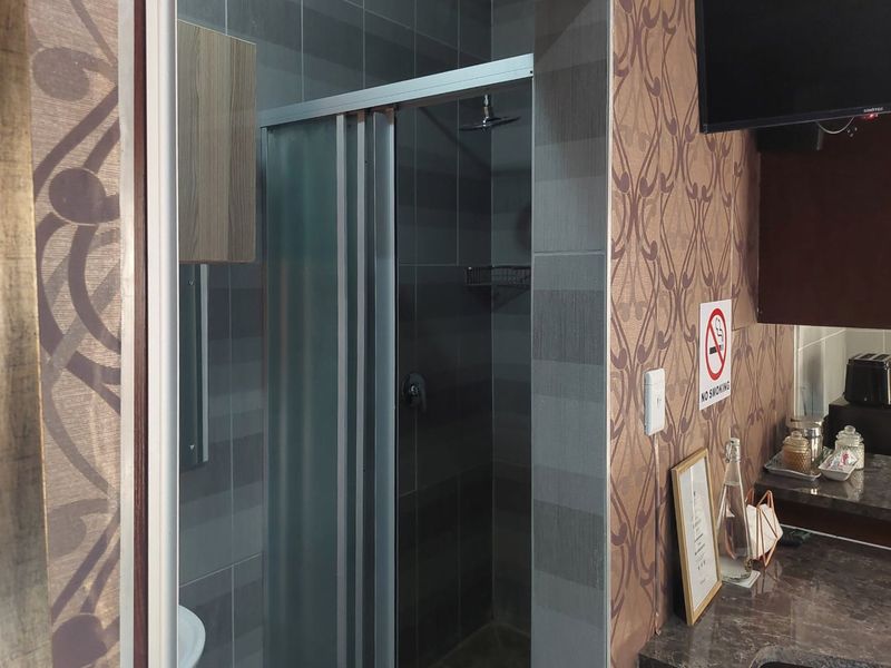 A compact bathroom featuring a tiled shower enclosure with a modern shower head and built-in shelving, integrated into the apartment layout.