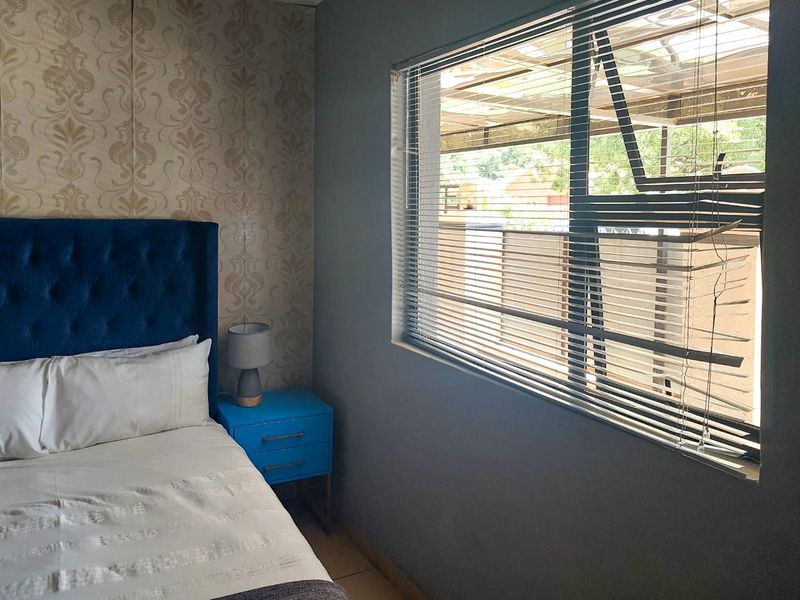 A bedroom featuring patterned wallpaper and an aluminium window fitted with venetian blinds.