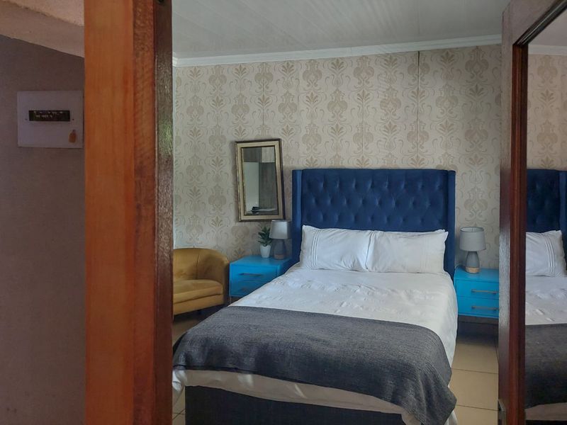 A bedroom featuring patterned wallpaper, tiled flooring, and a visible electrical distribution board, viewed through a doorway.